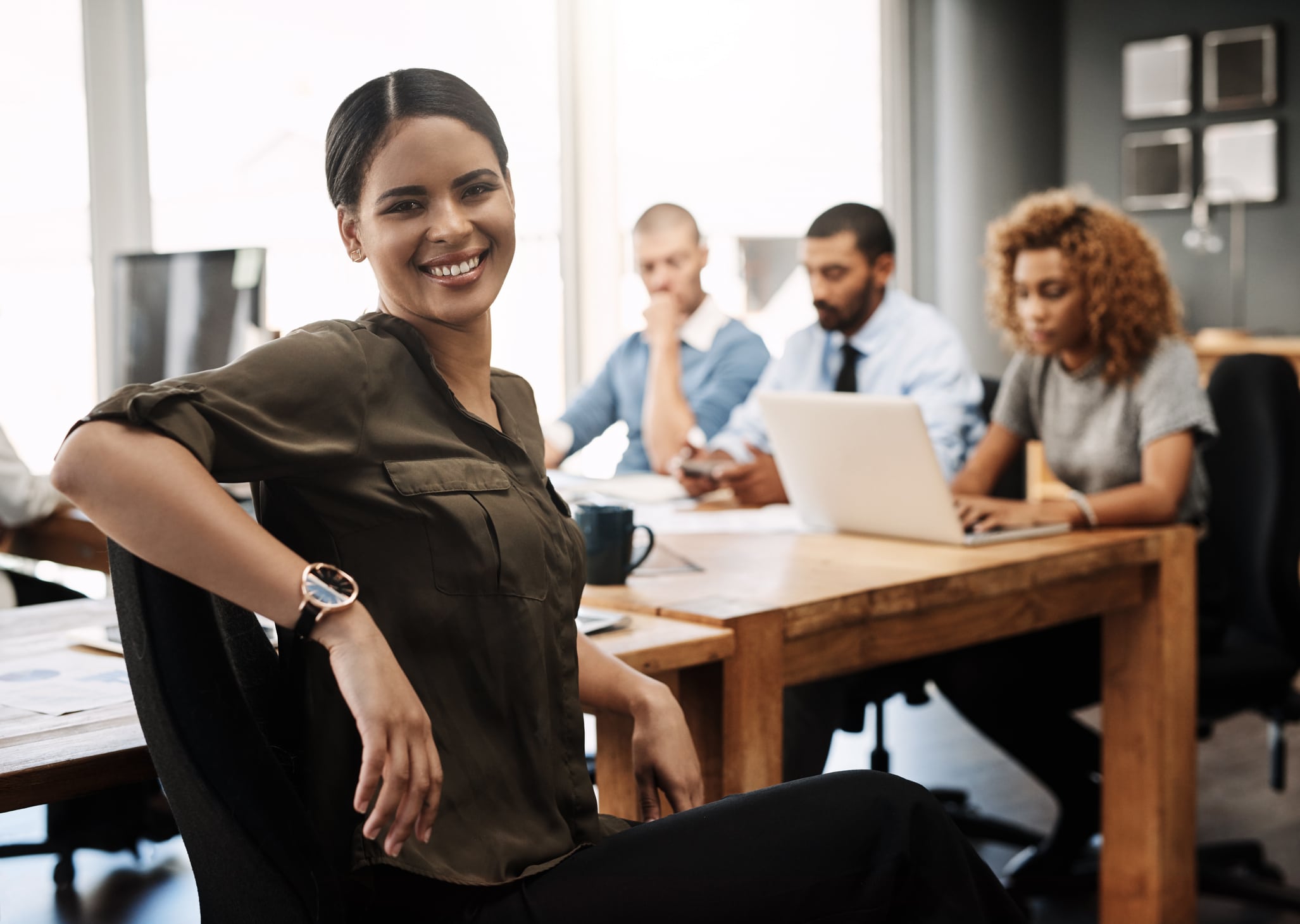 This is where we make success happen A smiling employee sits at a conference table with fellow workers.