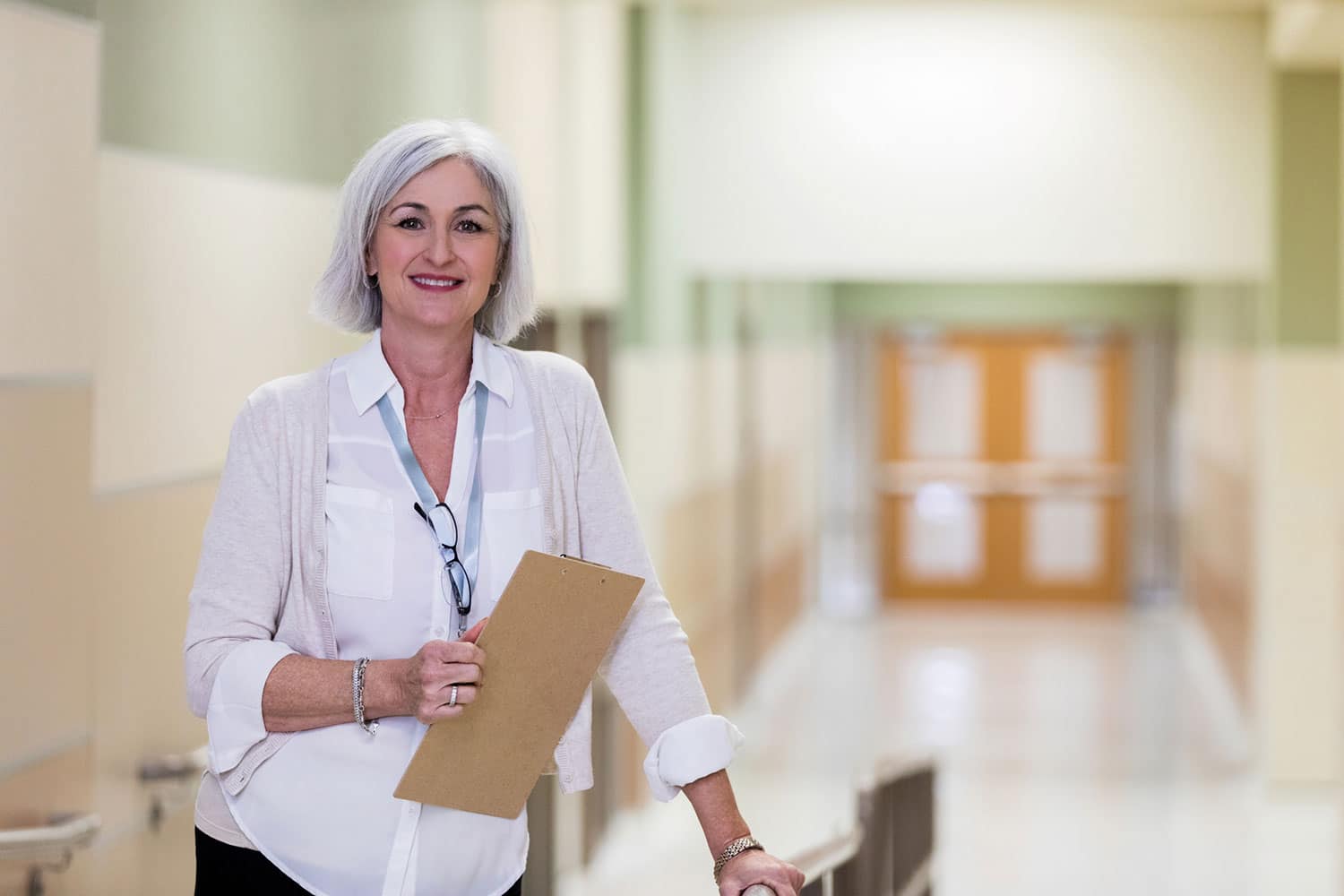 A long-term care administrator standing in the hallway of a facility with a clipboard.