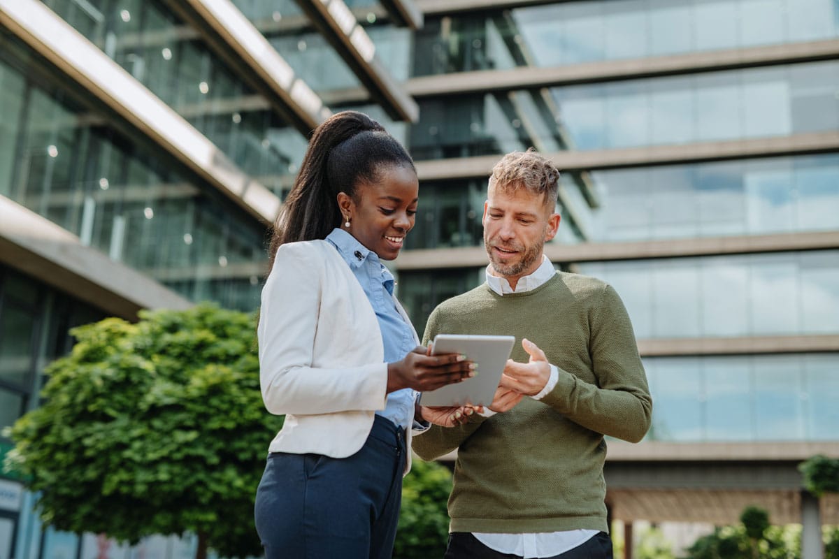 Two sustainability professionals review a tablet device next to an office building.