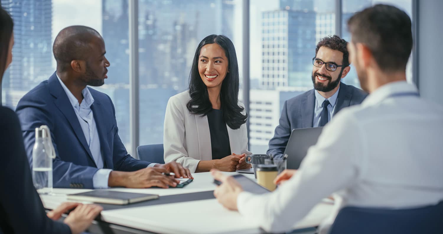 Smiling businesspeople meet around a conference table.