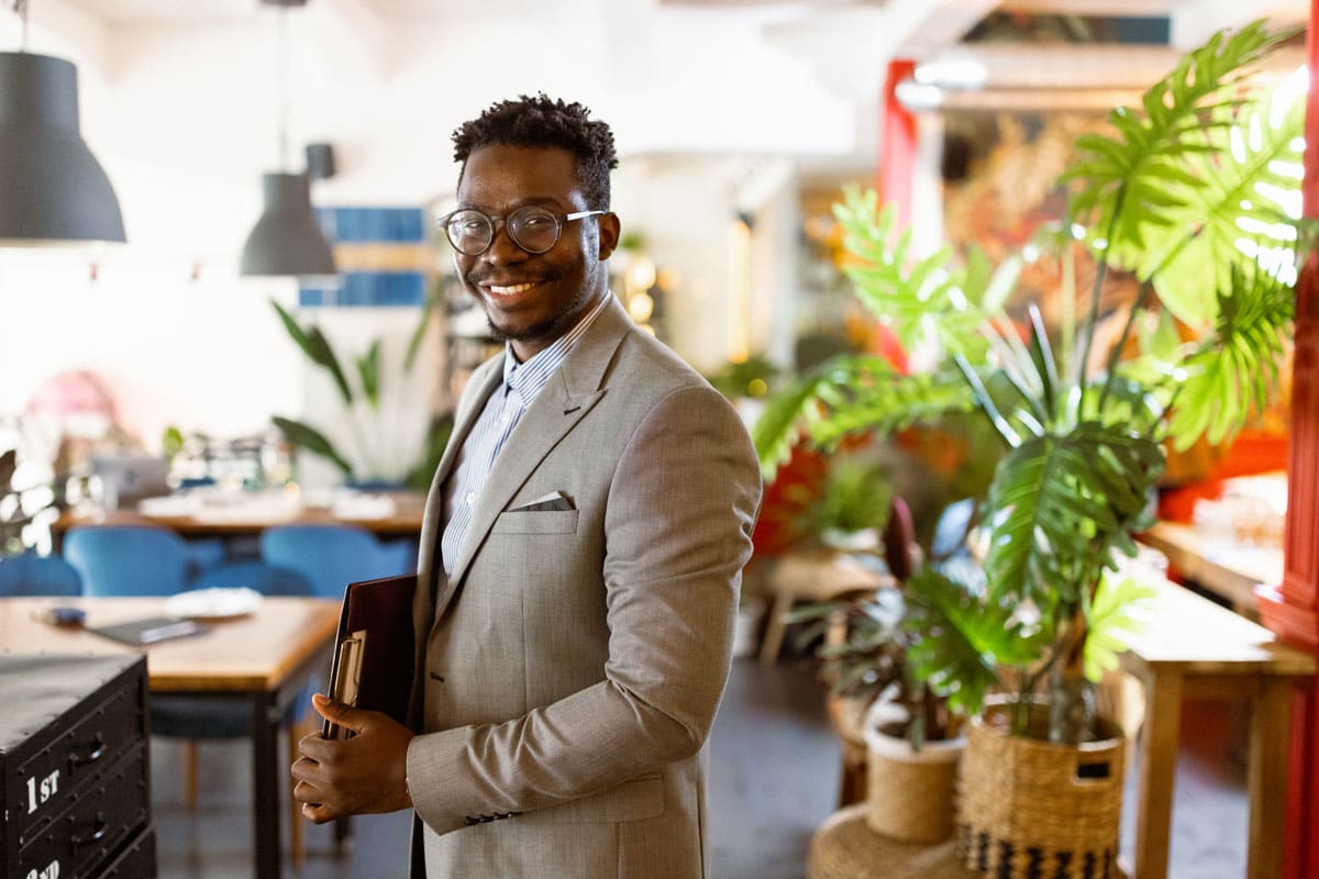 A sustainability professional stands in a room with plants, holding a clipboard.