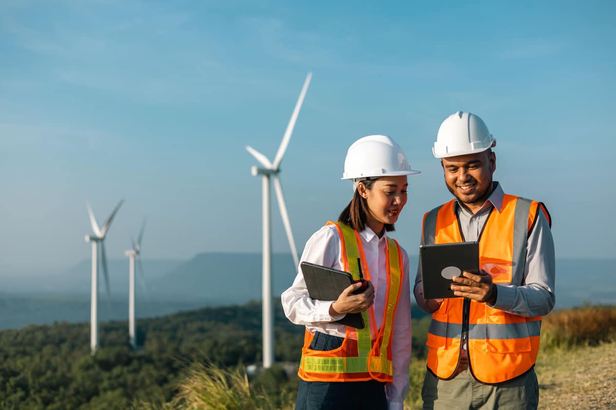 Two sustainability leaders with tablet computers standing in front of windmills.