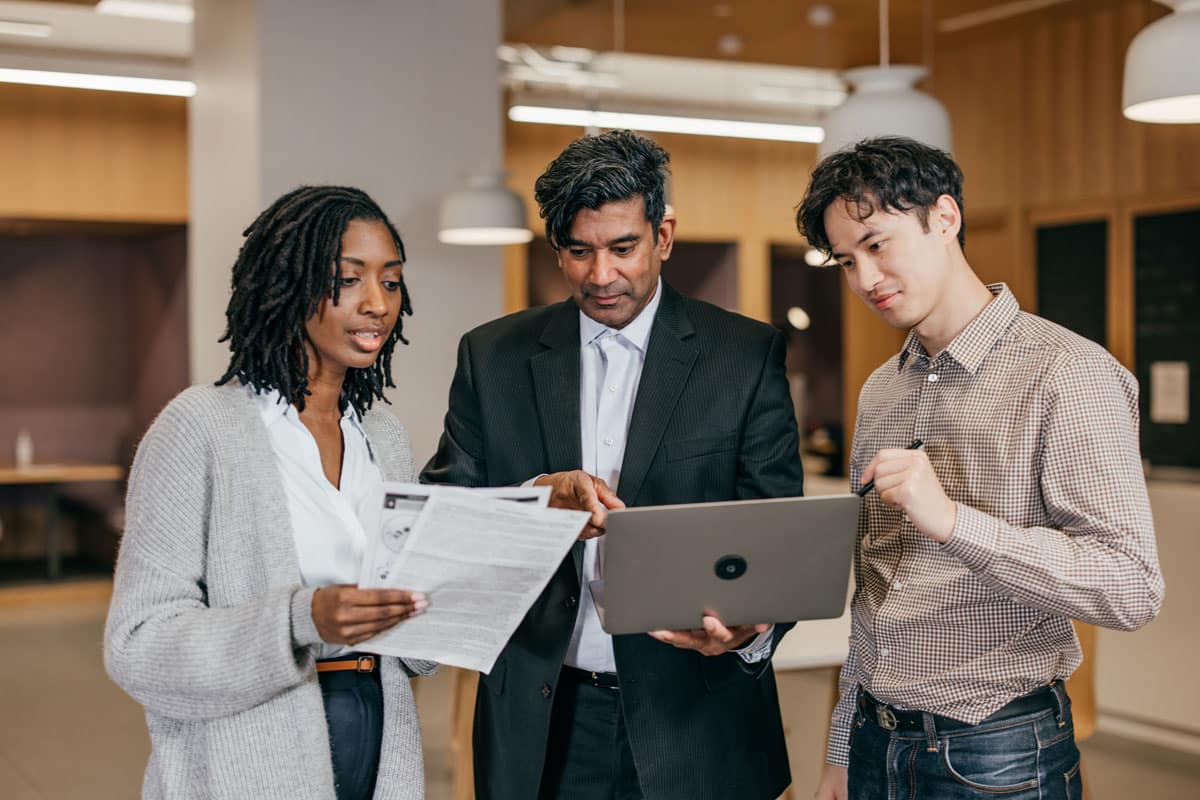 A human resources manager holding a laptop talks to two members of the HR team.
