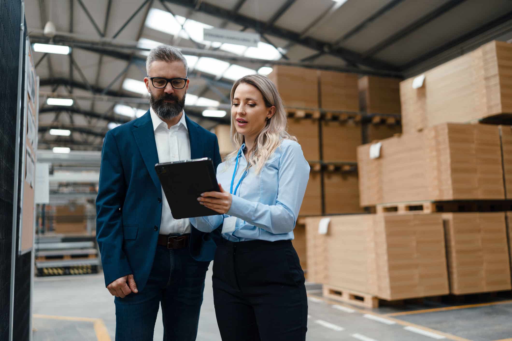 GettyImages-1902115709 An operations manager standing in a warehouse shows a colleague a tablet.