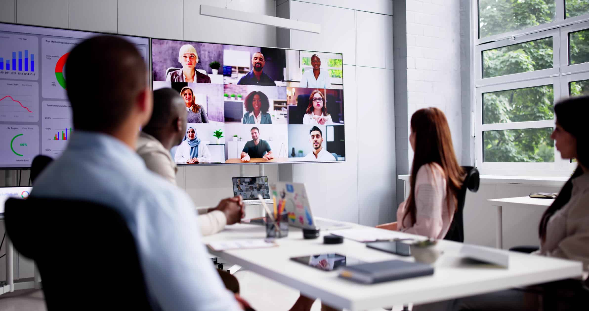 Online Video Conference Call A meeting between employees at a conference table and remote workers on a video screen.