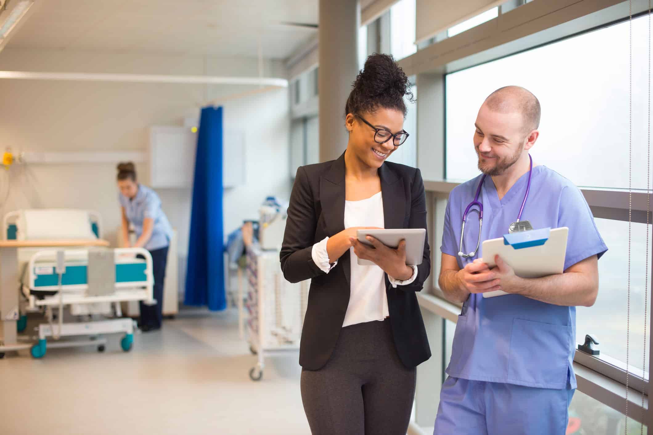 GettyImages-486265395 A hospital administrator shows a nurse a table in a hospital corridor.