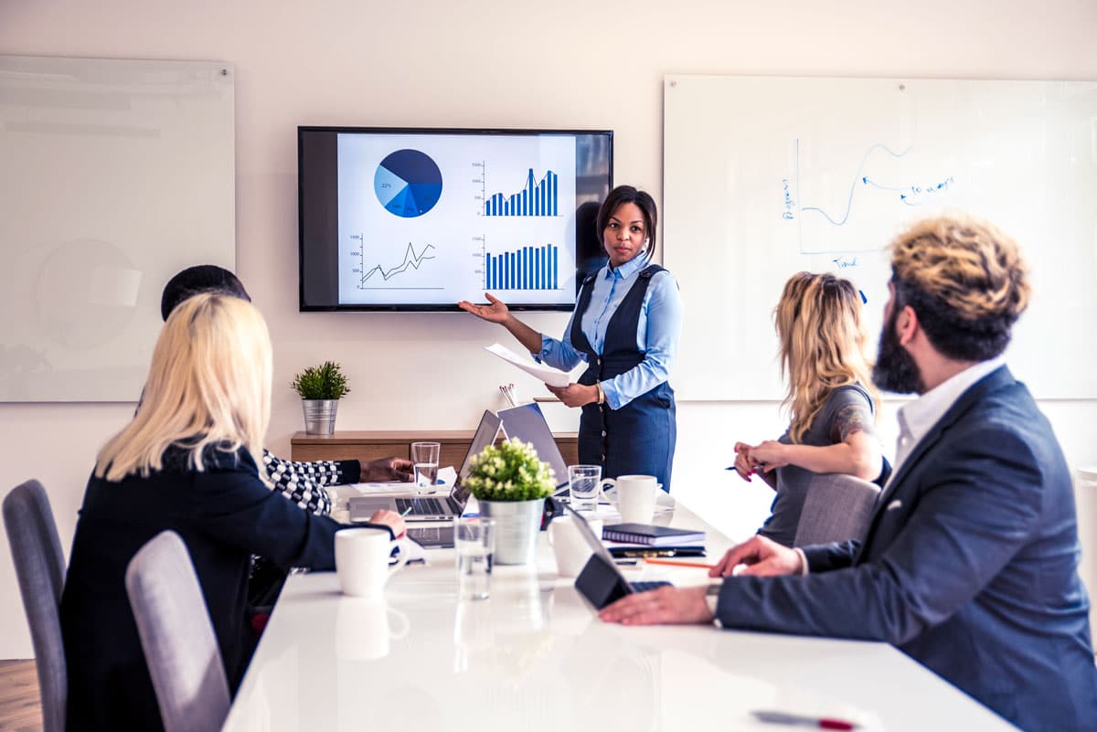 A management gives a presentation to colleagues sitting around a conference table.